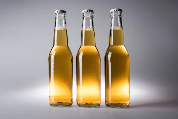 Three glass bottles with beer on grey background — Stock Photo