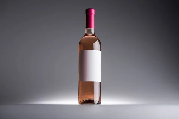 Botella de vino rosa y etiqueta en blanco sobre fondo oscuro con luz de fondo - foto de stock