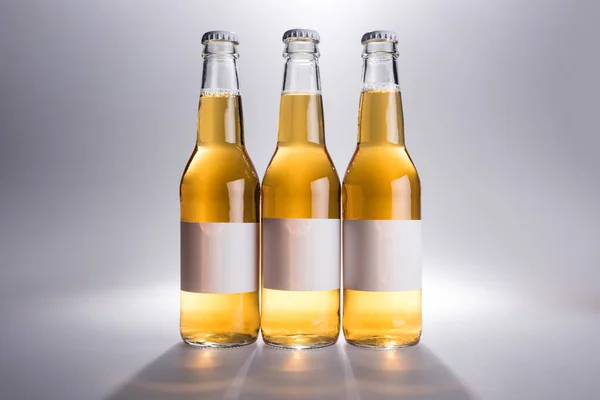 Three glass bottles with beer with white labels on grey background — Stock Photo