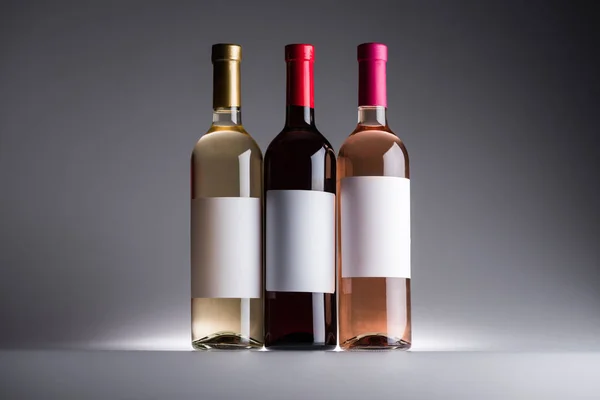 Bottles of red, white and rose wine with blank labels on dark background with back light — Stock Photo