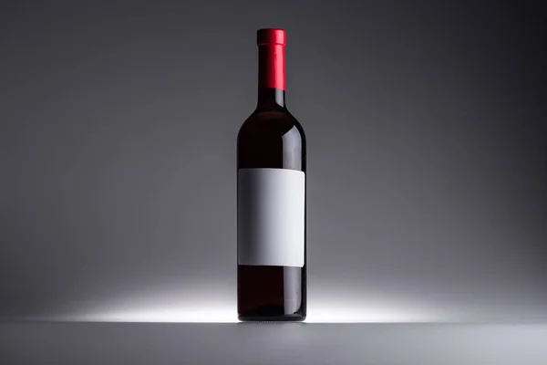 Flasche Rotwein und leeres Etikett auf dunklem Hintergrund mit Gegenlicht — Stockfoto