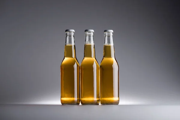 Tres botellas de vidrio con cerveza en fila sobre fondo gris con espacio para copiar - foto de stock