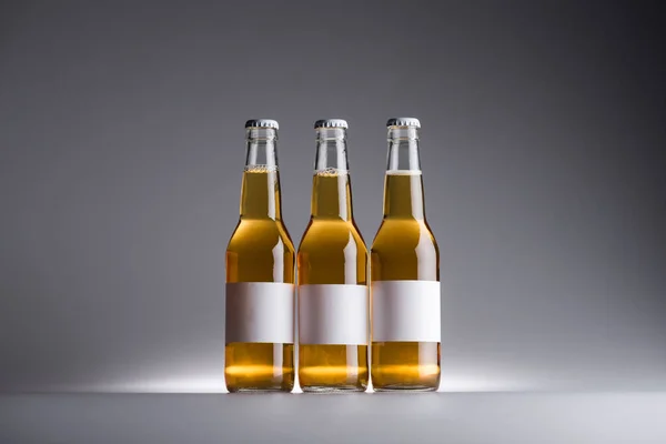 Tre bottiglie di vetro con birra ed etichette bianche in fila su sfondo scuro — Foto stock