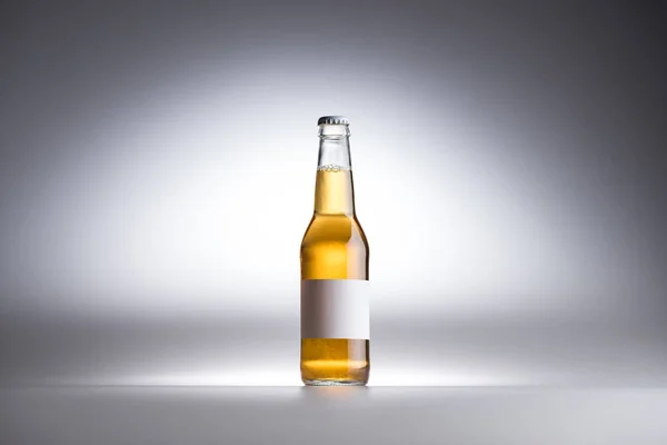 Botella de vidrio con cerveza y etiqueta blanca en blanco sobre fondo gris - foto de stock