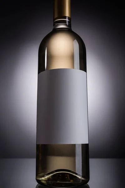 Low angle view of bottle with white wine and blank label on dark background with back light — Stock Photo