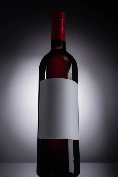 Vista ad angolo basso della bottiglia con vino rosso ed etichetta bianca su sfondo scuro con retroilluminazione — Foto stock