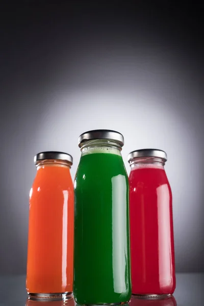 Vista de ángulo bajo de botellas con líquido colorido sobre fondo oscuro con luz de fondo - foto de stock