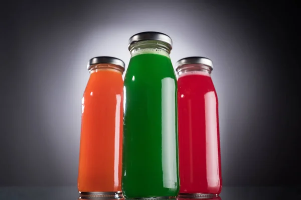 Vista de ángulo bajo de botellas de vidrio con líquido colorido sobre fondo oscuro con luz de fondo - foto de stock