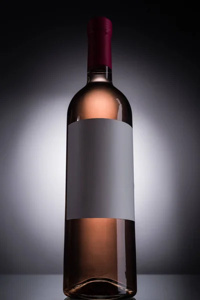 Vista en ángulo bajo de la botella con vino rosa y etiqueta en blanco sobre fondo oscuro con luz de fondo - foto de stock