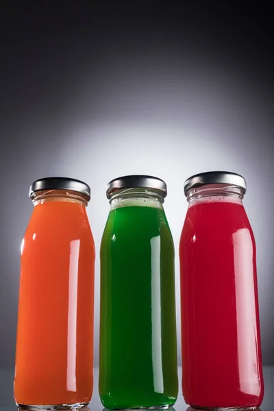 Vista de ángulo bajo de botellas de vidrio con líquido multicolor sobre fondo oscuro con luz de fondo - foto de stock