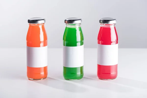 Ряд стеклянных бутылок с разноцветными жидкостными и белыми этикетками, изолированными на сером — стоковое фото