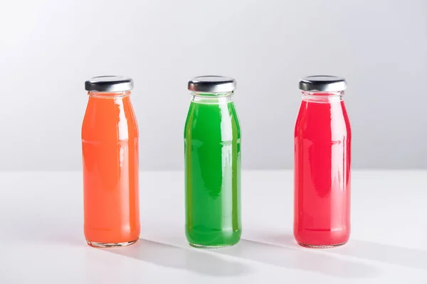 Ряд стеклянных бутылок с разноцветной жидкостью, изолированных на сером — стоковое фото