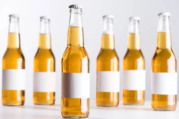 Focus selettivo di bottiglie di birra in vetro con etichette bianche bianche isolate su grigio — Foto stock