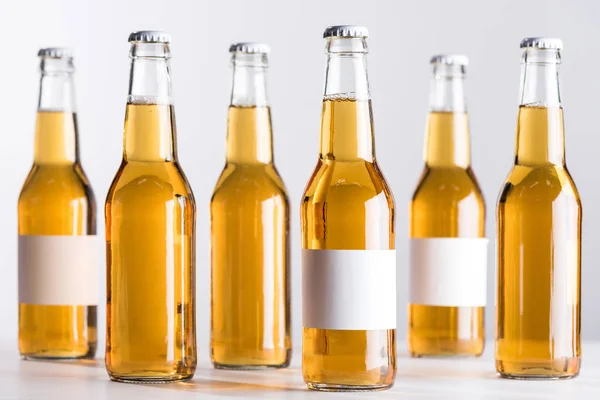 Селективный фокус бутылок пива с чистыми белыми этикетками, изолированными на сером — стоковое фото