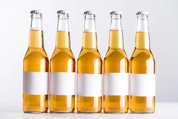 Cinco botellas de cerveza con etiquetas blancas en blanco aisladas en gris - foto de stock
