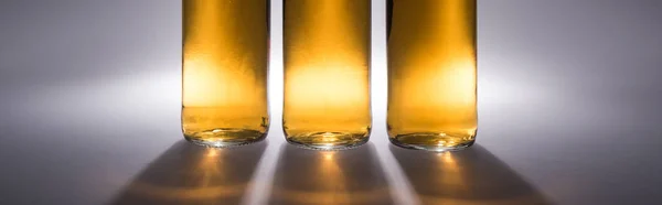 Vista de cerca de botellas de cerveza con luz y sombra sobre fondo gris, plano panorámico - foto de stock