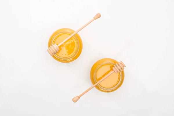 Top view of jars with honey and wooden honey dippers on white background — Stock Photo