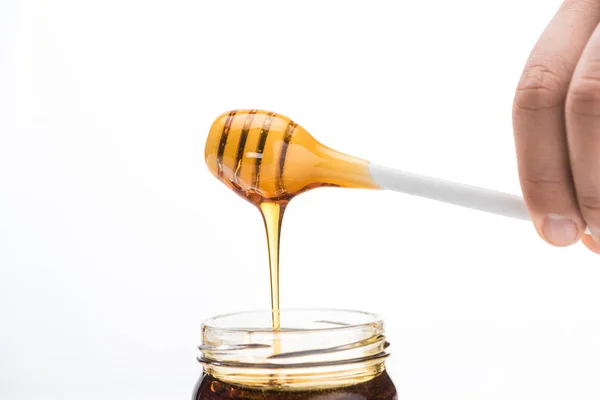 Cropped view of man holding honey dipper with dripping honey in jar isolated on white — Stock Photo