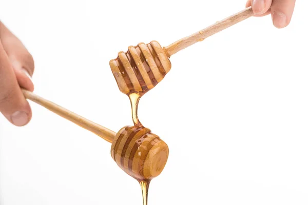 Cropped view of man holding wooden honey dippers with dripping honey isolated on white — Stock Photo