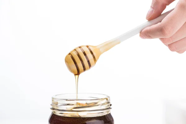 Visão parcial do homem segurando mel dipper com gotejamento de mel em frasco isolado em branco — Fotografia de Stock