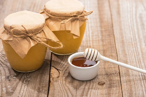 Gläser mit Honig in der Nähe von Schüssel und Honiglöffel auf Holztisch — Stockfoto