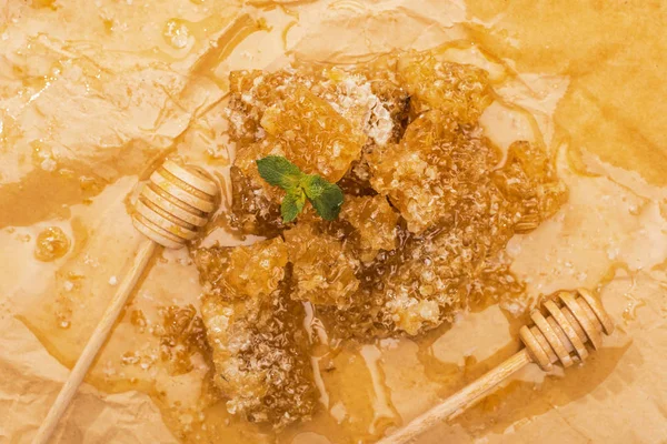 Вид сверху на соты и деревянные медовые ковши с мятными листьями в луже меда — стоковое фото