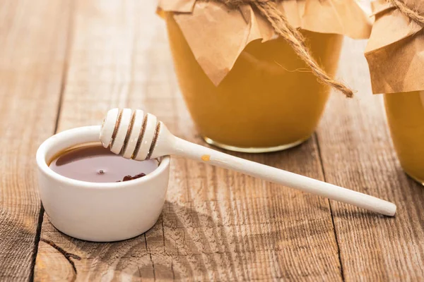 Jars with honey, bowl and honey dipper on wooden table in sunlight — Stock Photo