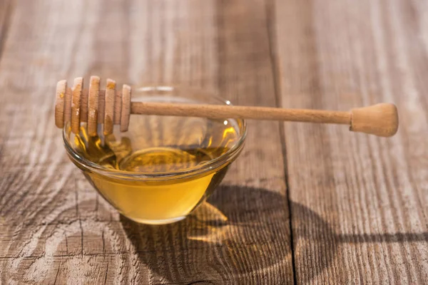 Glass bowl with tasty honey and honey dipper on wooden table in sunlight — Stock Photo