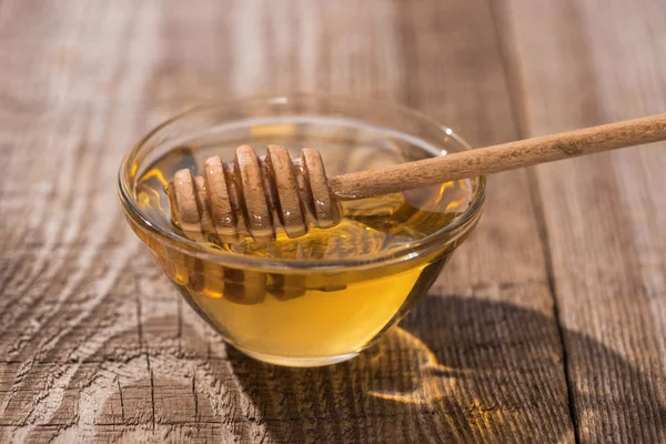 Tazón de vidrio con deliciosa miel y tarro de miel en mesa de madera a la luz del sol - foto de stock