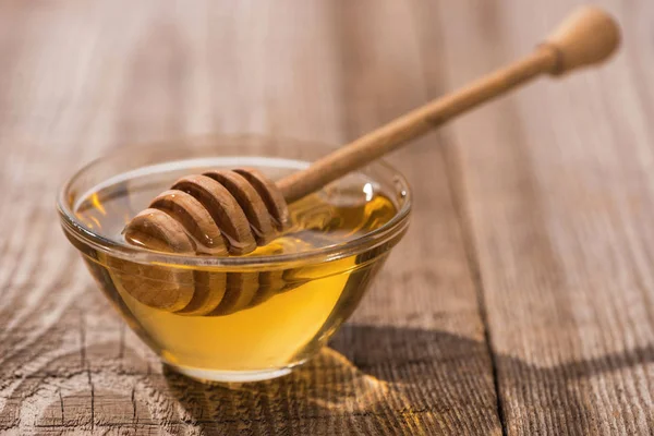 Glass bowl with sweet honey and honey dipper on wooden table in sunlight — Stock Photo
