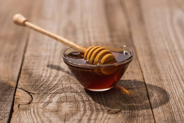 Glass bowl with honey and honey dipper on wooden table in sunlight — Stock Photo
