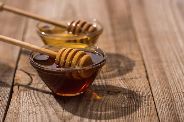 Selective focus of jars with honey and honey dippers on wooden table in sunshine — Stock Photo