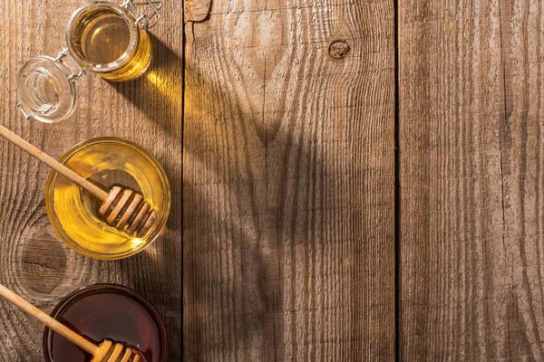 Draufsicht auf Gläser mit Honig und Honiglöffeln auf Holztisch bei Sonnenschein — Stockfoto