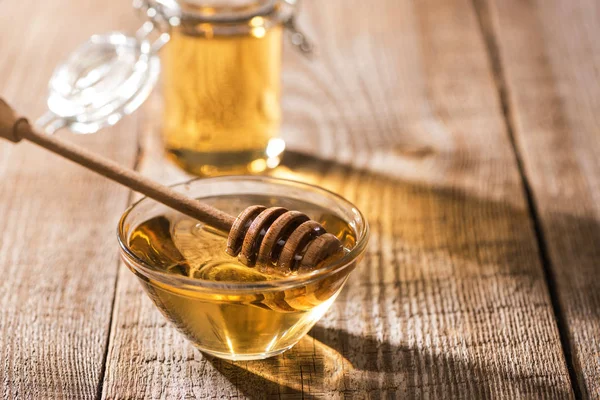 Jars with honey and honey dipper on wooden table in sunlight — Stock Photo