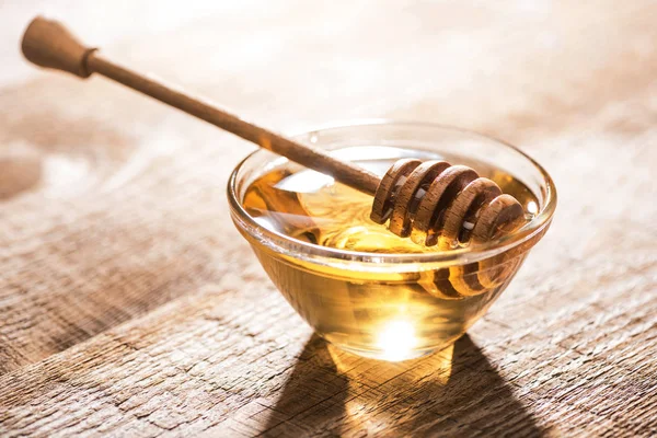 Jar with honey and honey dipper on wooden table in sunshine — Stock Photo