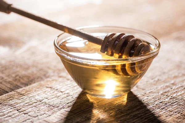 Jar with honey and honey dipper on wooden table in sunlight — Stock Photo