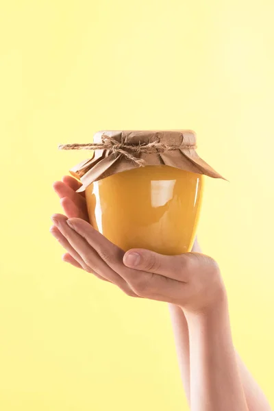 Vista parziale della donna che tiene in mano vaso di vetro con delizioso miele in mani isolate sul giallo — Foto stock