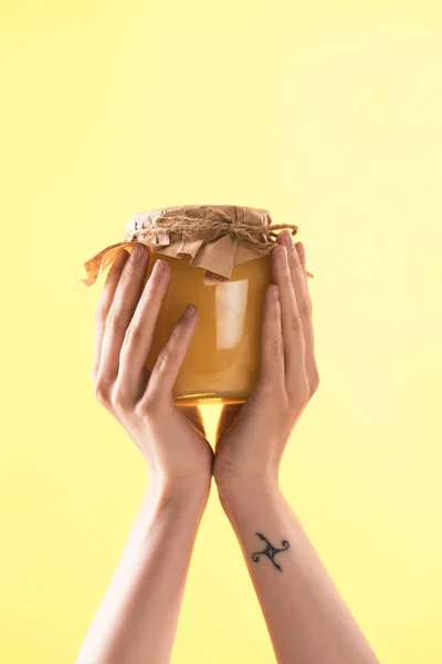 Vue recadrée de femme tenant un bocal en verre avec délicieux miel sucré isolé sur jaune — Photo de stock