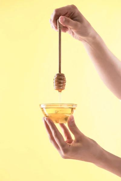 Cropped view of woman holding glass bowl and wooden dipper with dripping honey isolated on yellow — Stock Photo