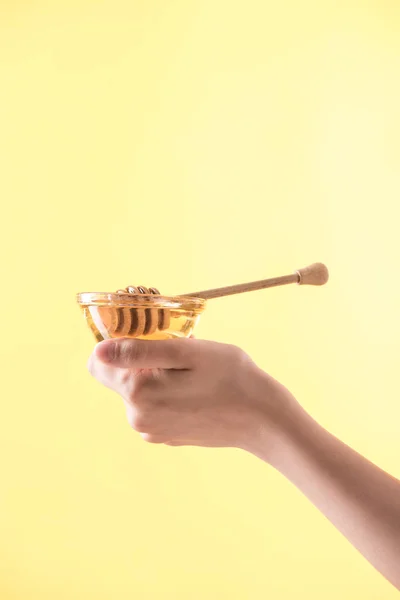 Partial view of woman holding glass bowl with honey and wooden dipper isolated on yellow — Stock Photo