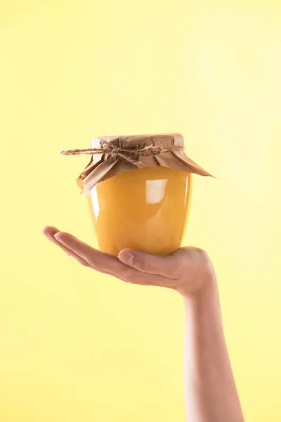 Partial view of woman holding glass jar with delicious honey isolated on yellow — Stock Photo