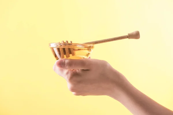 Vista ritagliata della donna che tiene ciotola di vetro con miele e scavo in legno isolato su giallo — Foto stock