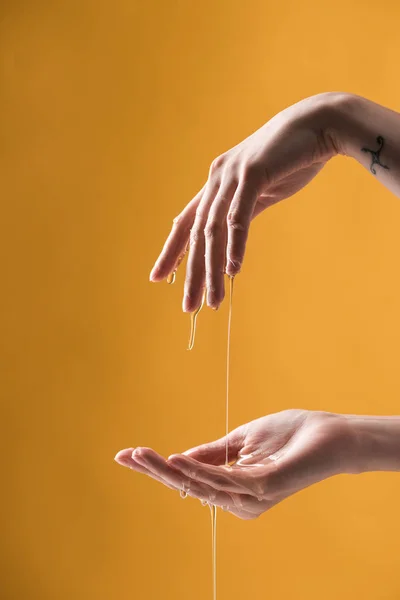 Cropped view of woman showing hands in dripping honey on orange background — Stock Photo