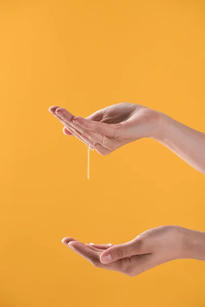 Vista ritagliata della donna che mostra le mani in gocciolante miele dolce isolato su arancione — Foto stock