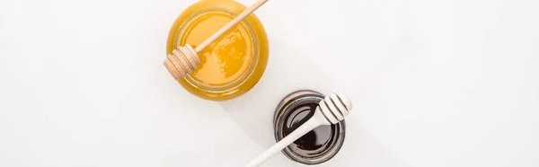 Panoramic shot of jars with honey and honey dippers on white background — Stock Photo