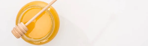 Panoramic shot of jar with honey and wooden dipper on white background — Stock Photo