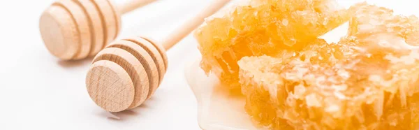 Panoramic shot of sweet honeycomb with honey near wooden honey dippers on white background — Stock Photo