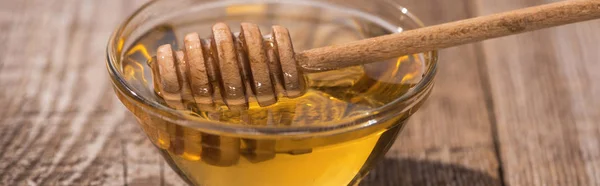 Panoramic shot of glass bowl with delicious honey and honey dipper on wooden table in sunlight — Stock Photo