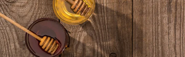 Tiro panorâmico de jarros com mel e mergulhadores de mel em mesa de madeira à luz solar — Fotografia de Stock