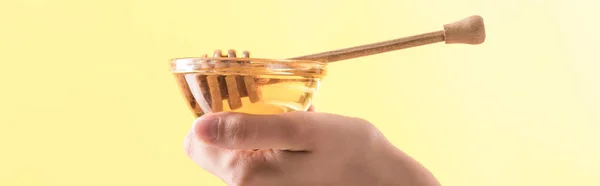 Partial view of woman holding glass bowl with honey and wooden dipper isolated on yellow, panoramic shot — Stock Photo